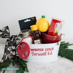 a winter cold survival kit sits in a white bucket on a marble countertop next to pine branches