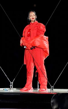 a woman standing on top of a stage with headphones in her ears and red outfit