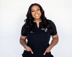 a woman in a black shirt is standing with her hands on her hips and smiling