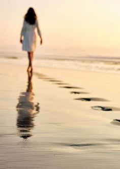 a woman walking on the beach at sunset