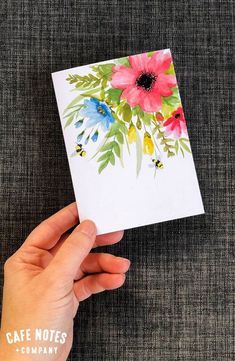 a hand holding a card with watercolor flowers on it