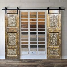 two wooden doors with decorative panels on the front and back, against a white brick wall