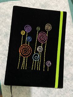 a black notebook with colorful flowers on the front and green line in the middle, sitting on top of a table