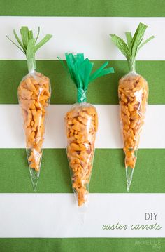 three plastic carrots with green tops on a striped tablecloth, one is made out of rice krispy kreme and the other two are shaped like carrots