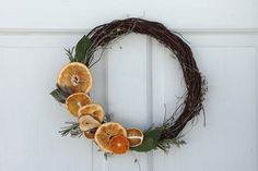 a grapevine wreath with dried oranges and leaves hanging on the front door,