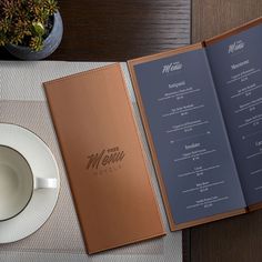 an open menu sitting on top of a table next to a cup and saucer