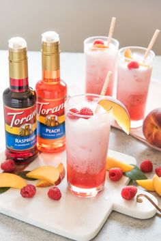 two glasses filled with raspberry lemonade punch and three bottles of torani