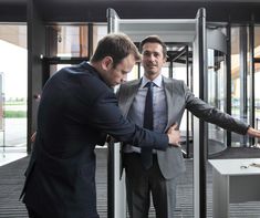 two men in suits are looking at something on the floor near a glass door that is open