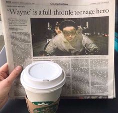 a person holding up a newspaper with a cup of coffee in front of them