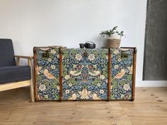 an old suitcase sitting on top of a wooden floor next to a chair and potted plant