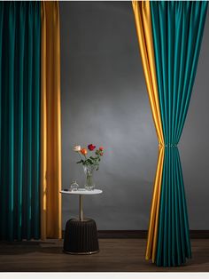 a vase with flowers sitting on top of a table next to a curtained window