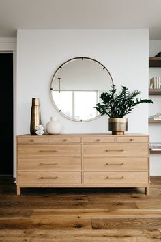 a wooden dresser with a round mirror on it's wall above it and a potted plant in front of it