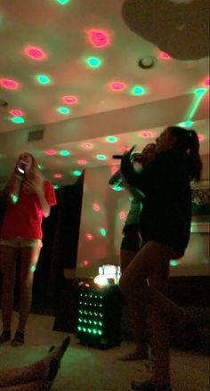 two girls are singing into microphones in a room with lights on the ceiling