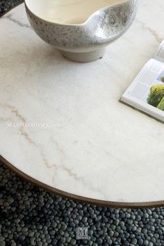 a table with a magazine on top of it next to a bowl and cup sitting on the coffee table