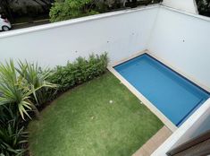 an above ground swimming pool surrounded by lush green plants and shrubs, with a car parked in the background