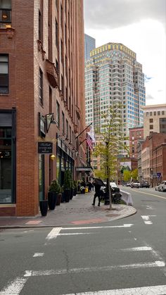 an empty city street with tall buildings in the back ground and people walking on the sidewalk