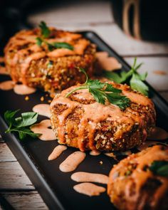 three meat patties covered in sauce and garnished with parsley on a black plate