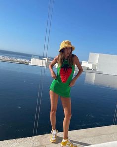 a woman in a green dress and straw hat standing on the edge of a pier