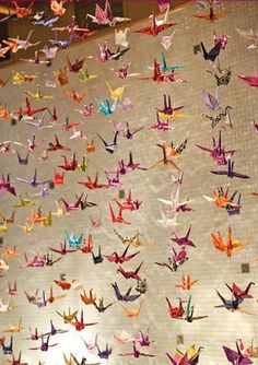 many colorful origami birds are flying in the air on a sheet of paper