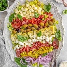 a large salad with olives, tomatoes, lettuce and other ingredients on a white platter