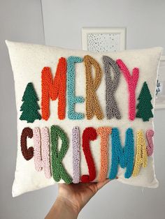 someone is holding up a pillow with the words merry christmas written in crochet