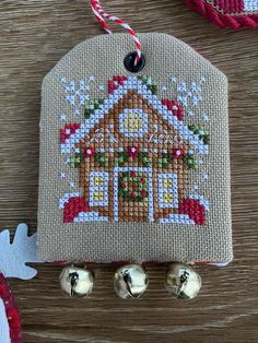 a cross stitch ornament hanging from a wooden table next to bells and decorations