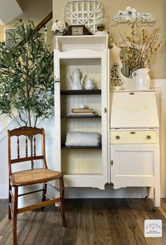 an old china cabinet is decorated with white flowers and greenery, while a wooden chair sits in front of it