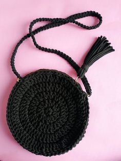 a black crocheted purse with a tasseled handle on a pink surface