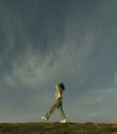 a woman is flying a kite in the air on top of a grassy hill under a cloudy blue sky