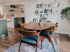 a dining room table with blue chairs and pictures on the wall above it, in front of an open kitchen