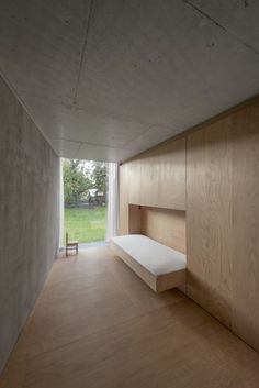 an empty room with wood paneling and white bed in the center, looking out onto a grassy field