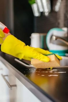 a person in yellow gloves is cleaning a kitchen sink with sponges and a rag