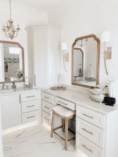 a white bathroom with marble counter tops and two mirrors on the wall, along with stools