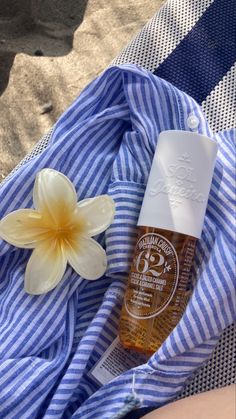 a bottle of sunscreen next to a flower on a blue and white striped towel