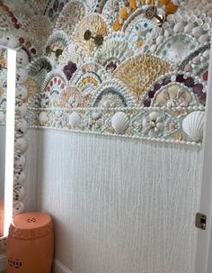 this bathroom has shells on the wall and an orange stool in front of it,