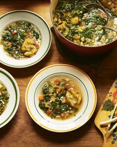 four bowls filled with soup and vegetables on top of a wooden table next to utensils