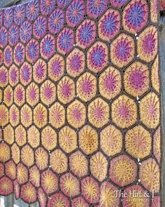 a crocheted blanket hanging on the side of a wooden fence with purple and yellow flowers