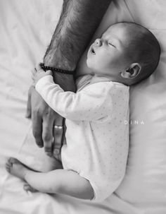 a black and white photo of a baby sleeping on a bed with his arm around an adult's leg