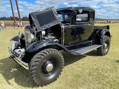 an old black truck parked on top of a grass covered field