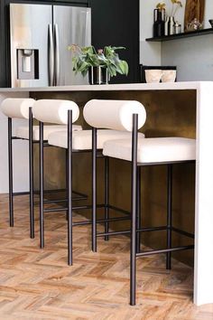 three white bar stools sitting in front of an island