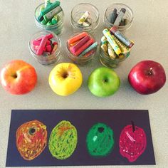 an assortment of different colored crayons and apples on a table next to pencils