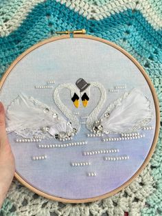 a hand is holding a cross - stitch hoop with two swans on it