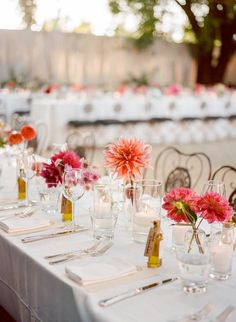 the table is set with white linens and pink flowers in vases on each side