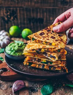 a hand holding a stack of quesadillas on a plate with guacamole