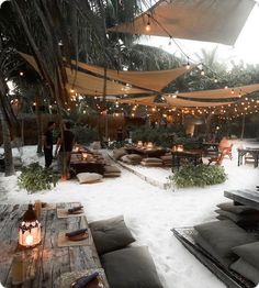 an outdoor seating area is covered in snow and lit by string lights, surrounded by palm trees