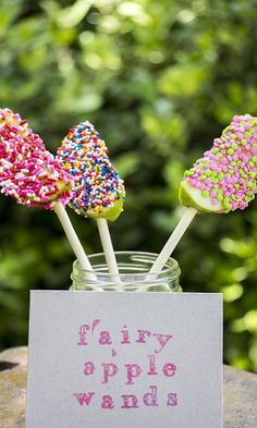 three candy lollipops sitting in a jar with a sign on it that says fairy apple wands