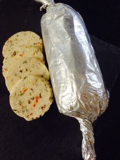 some food is wrapped in tin foil on a black counter top with a piece of bread