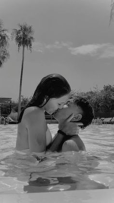 a man and woman are kissing in the swimming pool with palm trees on either side