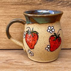 a ceramic mug with strawberries painted on the side and flowers in the middle, sitting on a wooden surface