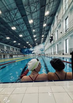 two women are sitting in the middle of an indoor swimming pool while looking out at the water